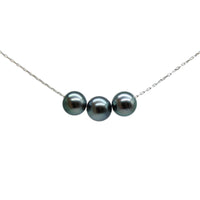 A delicate silver chain necklace featuring three colorful black pearls aligned horizontally in the center, set against a solid light gray background.