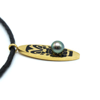 Necklace with a gold pendant featuring a black design and a pearl on a white background