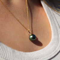Necklace with a green pearl pendant worn by a person in a light gray shirt.