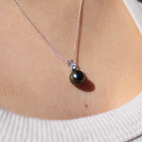 Model wearing a white gold and lab grown diamond pendant featuring a black pearl