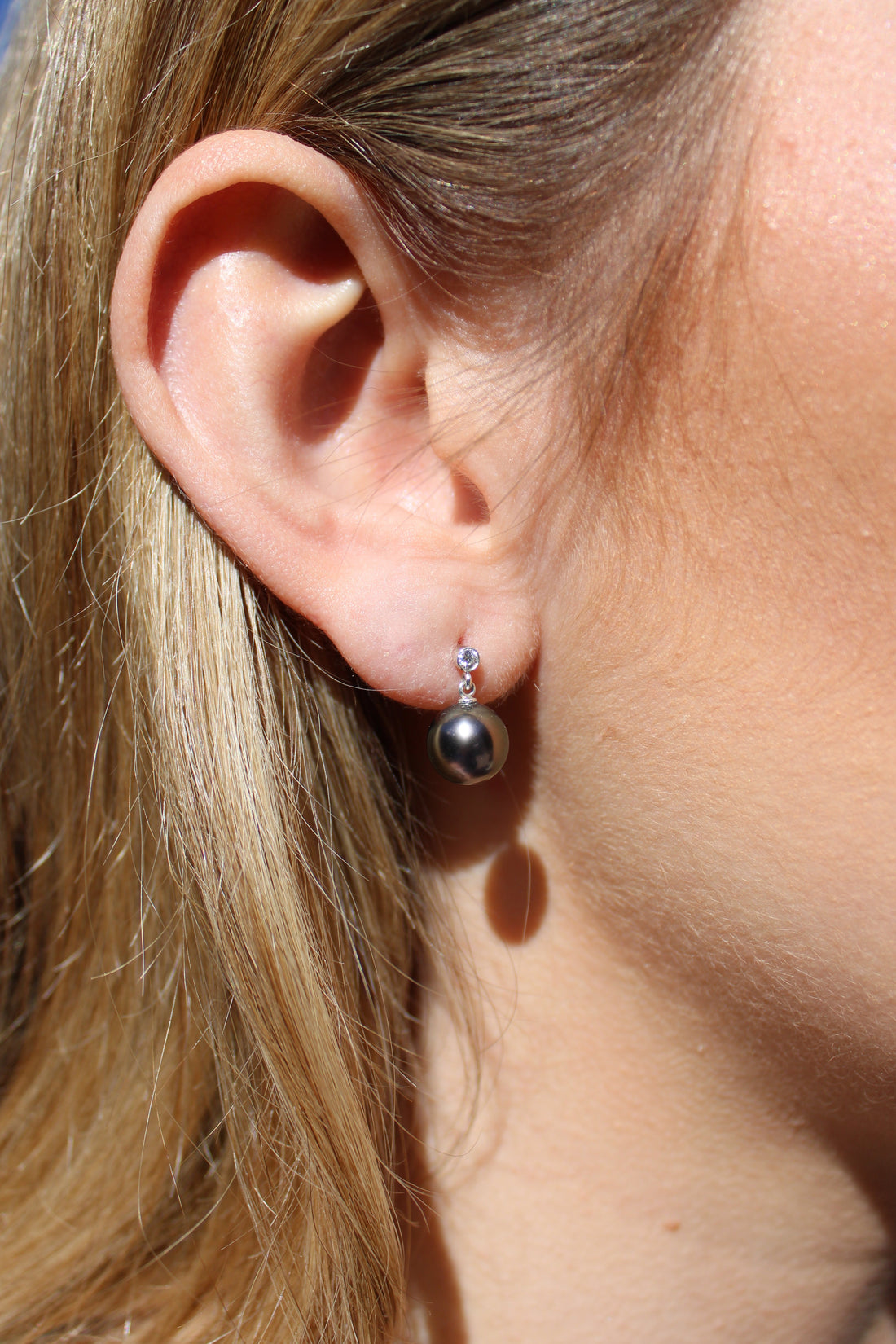 Close-up of a person wearing a sterling silver dangly earrings with a black pearl and a moissanite gem