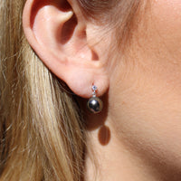 Close-up of a person wearing a sterling silver dangly earrings with a black pearl and a moissanite gem