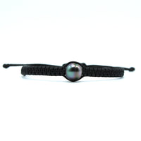 A black macrame bracelet featuring a central iridescent black pearl, set against a plain white background.