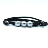 A black leather bracelet featuring three smooth, lustrous gray pearls in the center, flanked by small silver-toned metal beads, set against a plain white background.