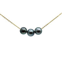 A delicate gold chain necklace featuring three colorful black pearls aligned horizontally in the center, set against a clean light gray background.
