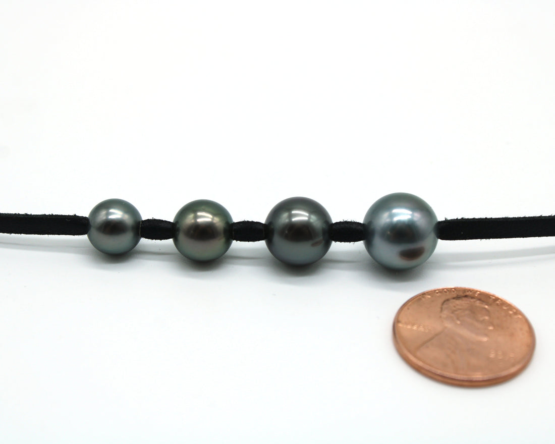 Tahitian black pearl size comparison — 8mm, 9mm, 10mm, and 11mm pearls on leather cord with penny for scale
