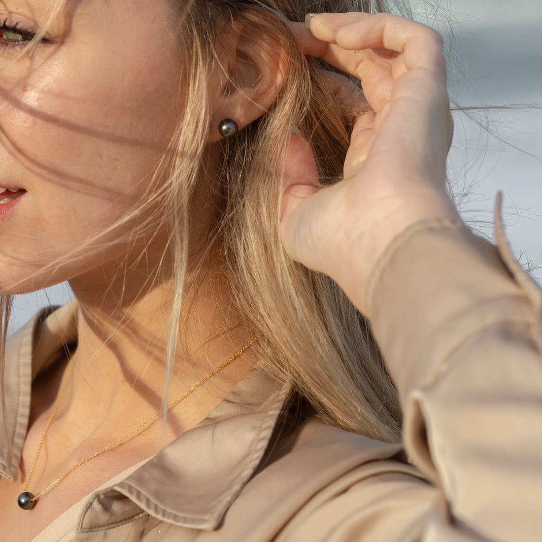Photo of a woman wearing a pair of Tahitian Black Pearl studs and a gold floating Tahitian Pearl Necklace.