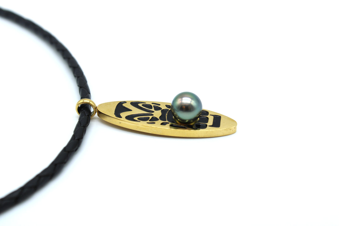 Necklace with a gold pendant featuring a black design and a pearl on a white background