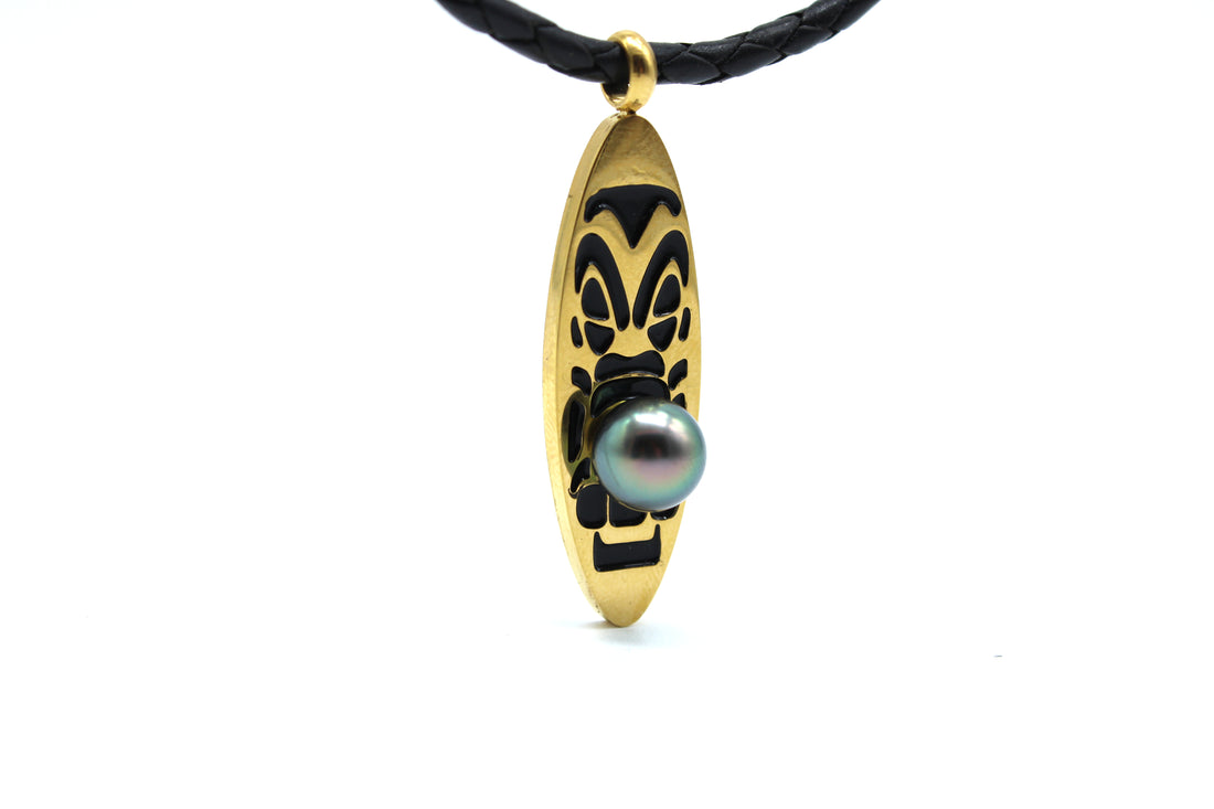 Gold pendant with black design and a black pearl on a white background