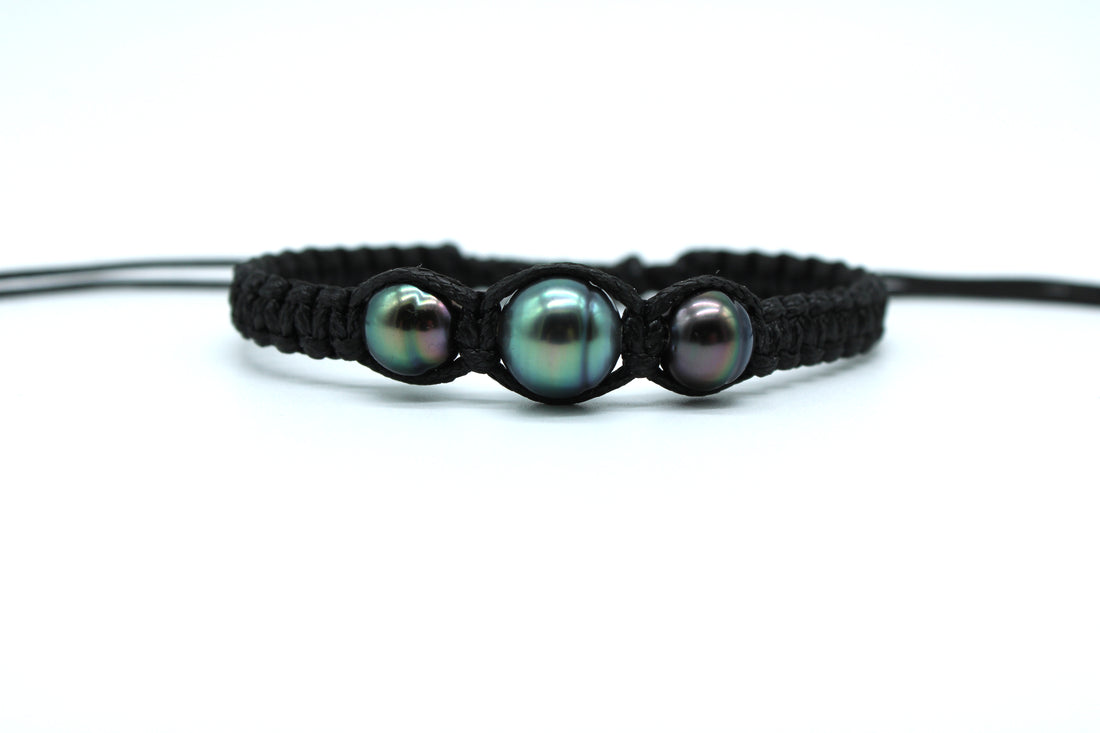 Black braided bracelet with three pearls on a white background