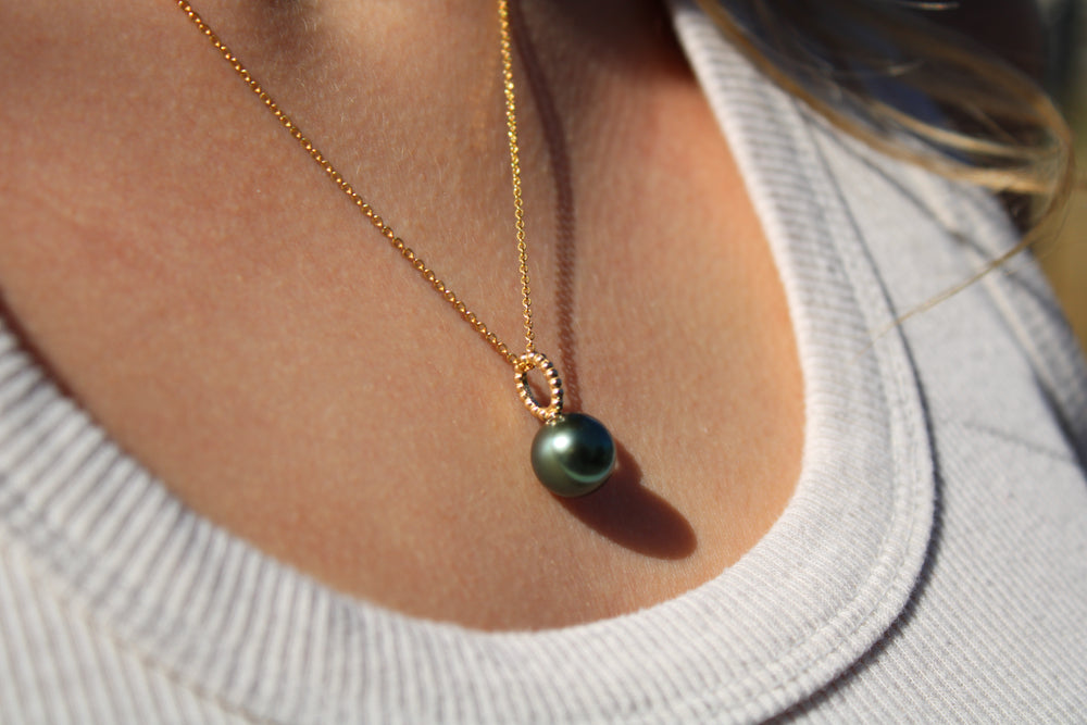 Necklace with a green pearl pendant worn by a person in a light gray shirt.