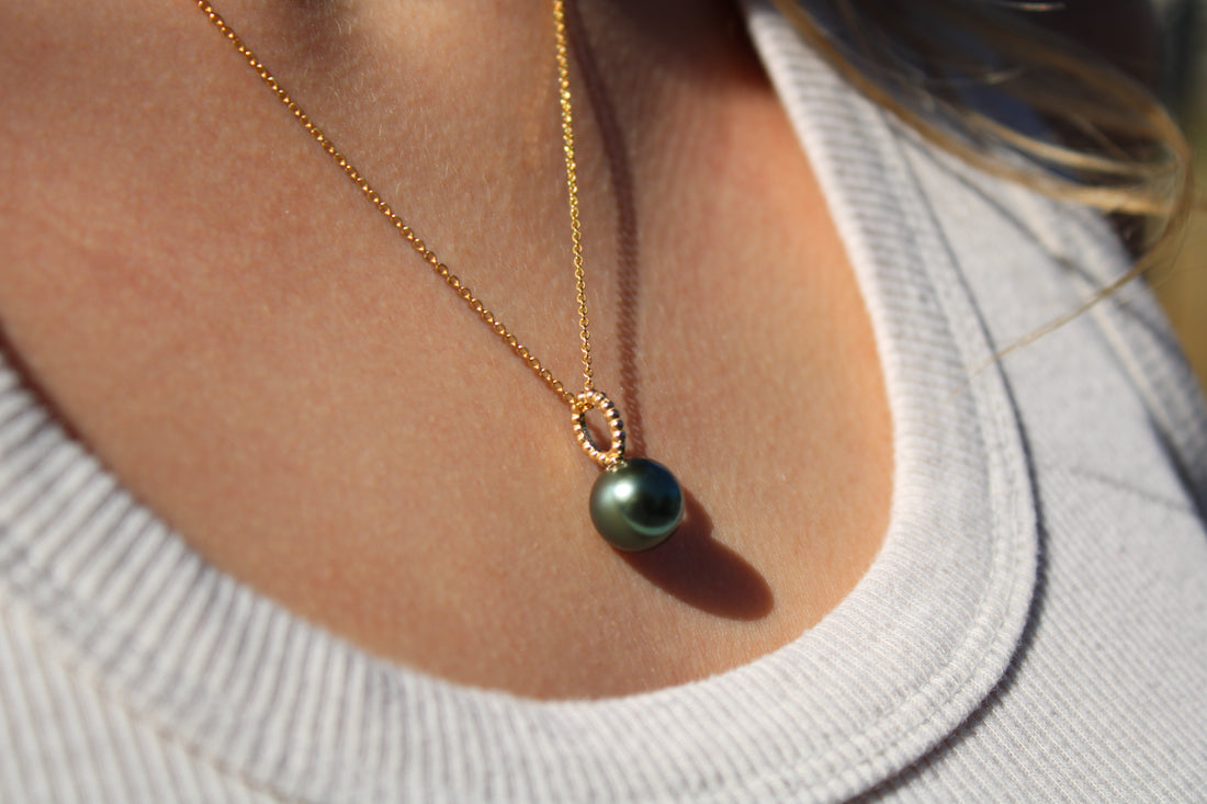 Necklace with a green pearl pendant worn by a person in a light gray shirt.