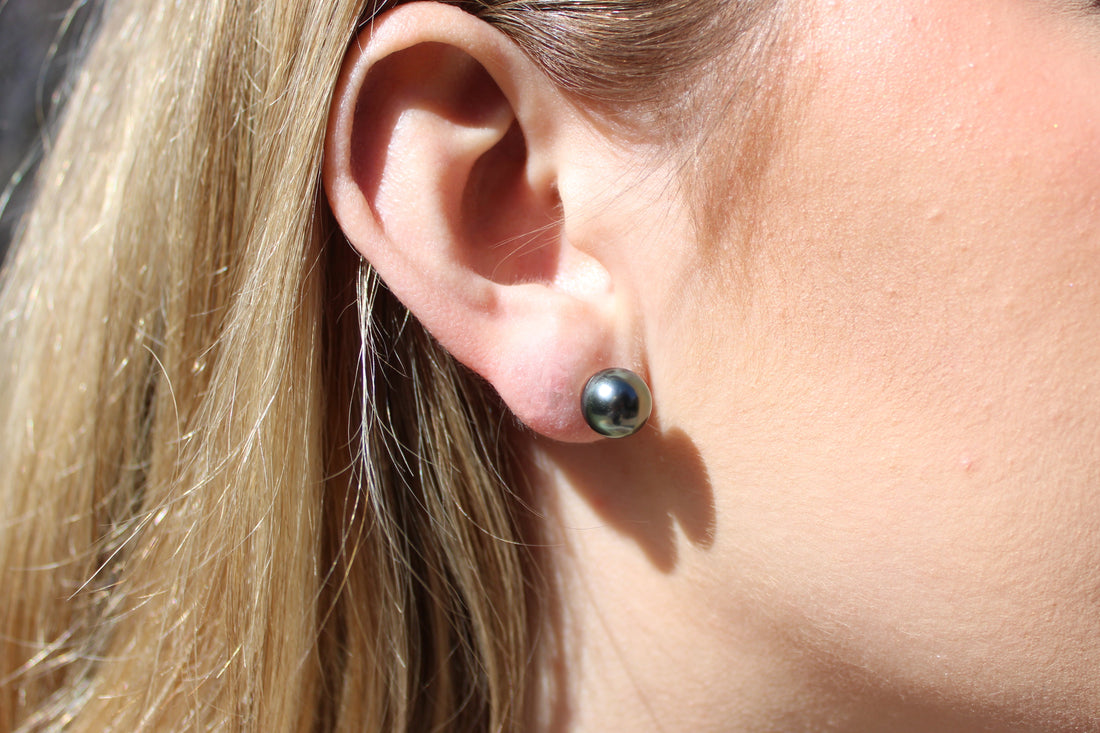 Close-up of a person wearing a black pearl stud earring.