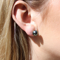 Close-up of a person wearing a black pearl stud earring.