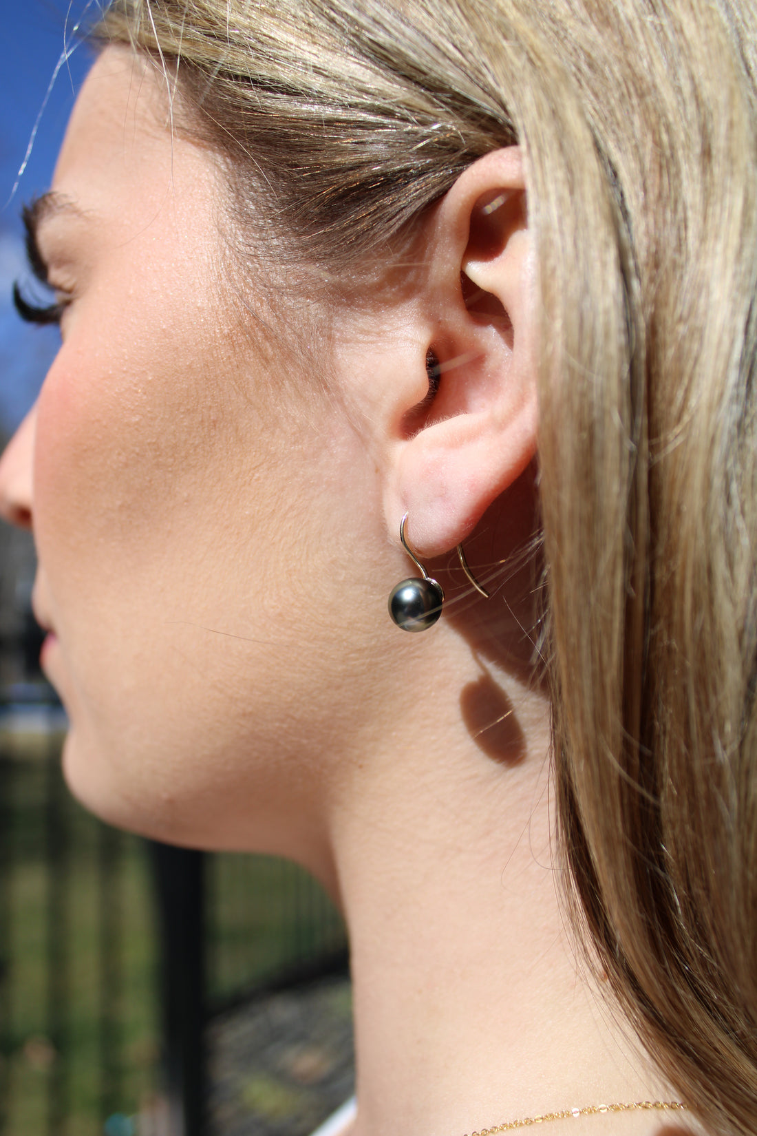 Close-up of a person wearing a white gold black pearl french hook earring outdoors