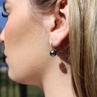 Close-up of a person wearing a white gold black pearl french hook earring outdoors