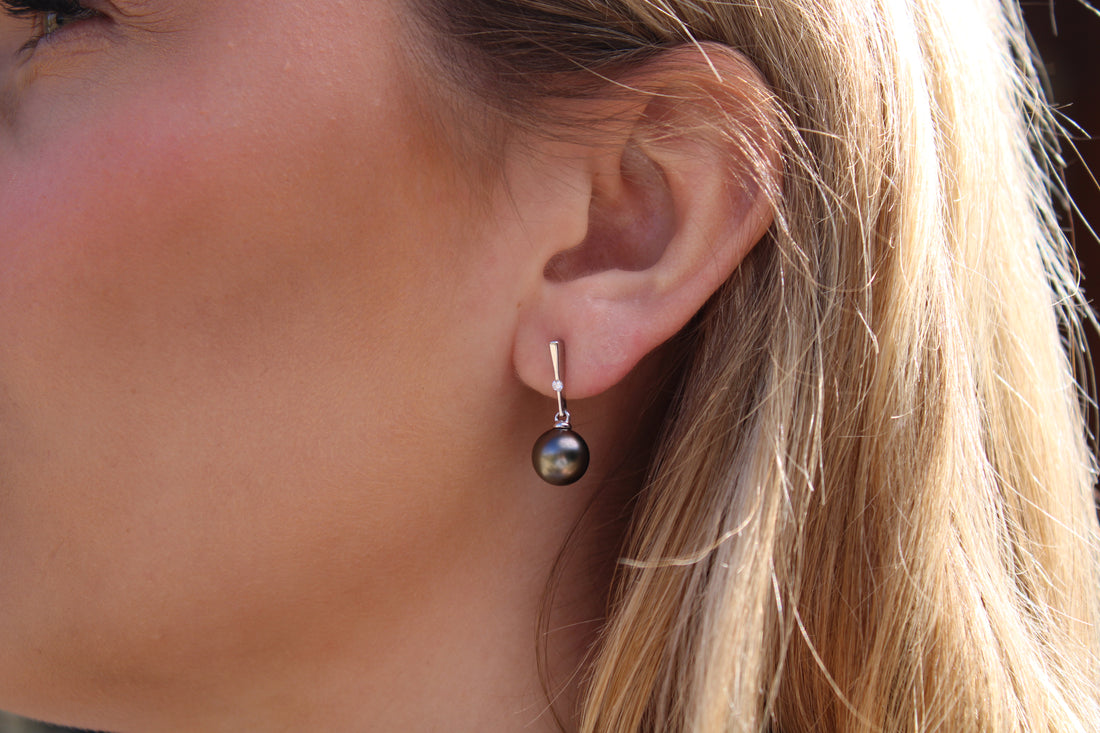Close-up of a person wearing a black pearl earring with white gold and lab grown diamonds with a blurred background