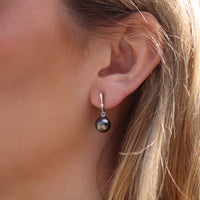 Close-up of a person wearing a black pearl earring with white gold and lab grown diamonds with a blurred background
