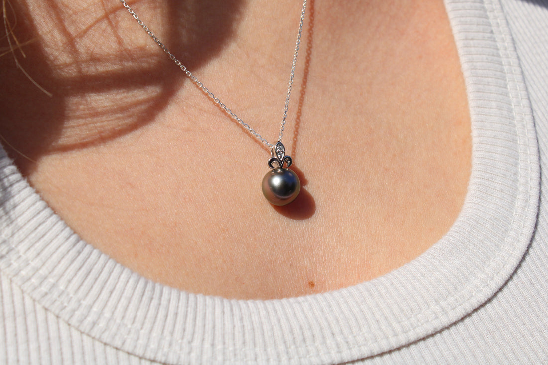 Close-up of a necklace with a white gold fleur de lis black pearl pendant on a person wearing a white sweater.