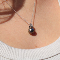 Close-up of a necklace with a white gold fleur de lis black pearl pendant on a person wearing a white sweater.