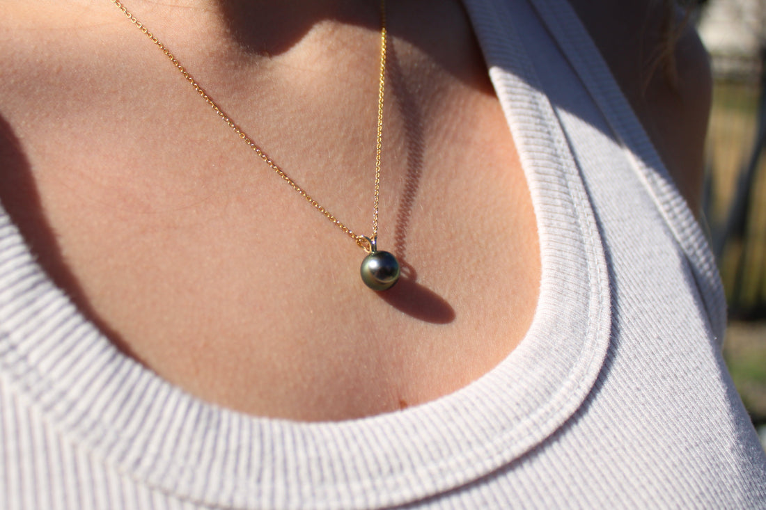 Close up of someone wearing a necklace with a yellow gold pendant featuring a black pearl 