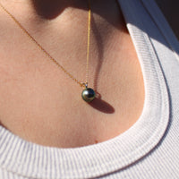 Close up of someone wearing a necklace with a yellow gold pendant featuring a black pearl 