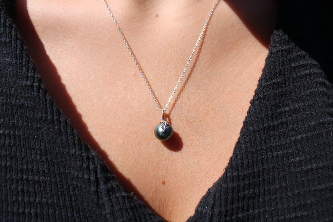 Close up of a person wearing a necklace with a black pearl pendant