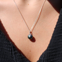 Close up of a person wearing a necklace with a black pearl pendant