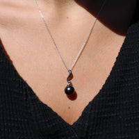 Model wearing a sterling silver necklace featuring a swirl shaped pendant with  black pearl 