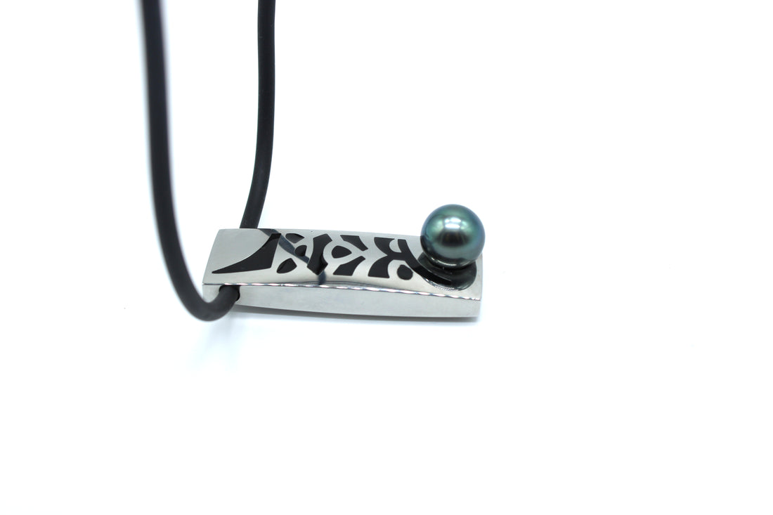 Necklace with a rectangular pendant featuring a black and silver pattern and a green pearl on a white background