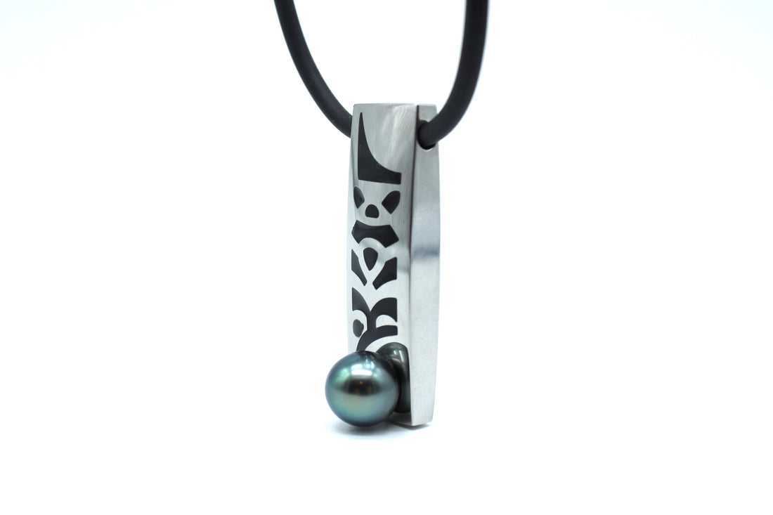 Necklace with a rectangular pendant featuring a pattern and a central black pearl on a white background