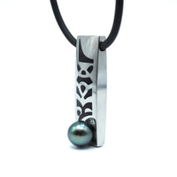 Necklace with a rectangular pendant featuring a pattern and a central black pearl on a white background