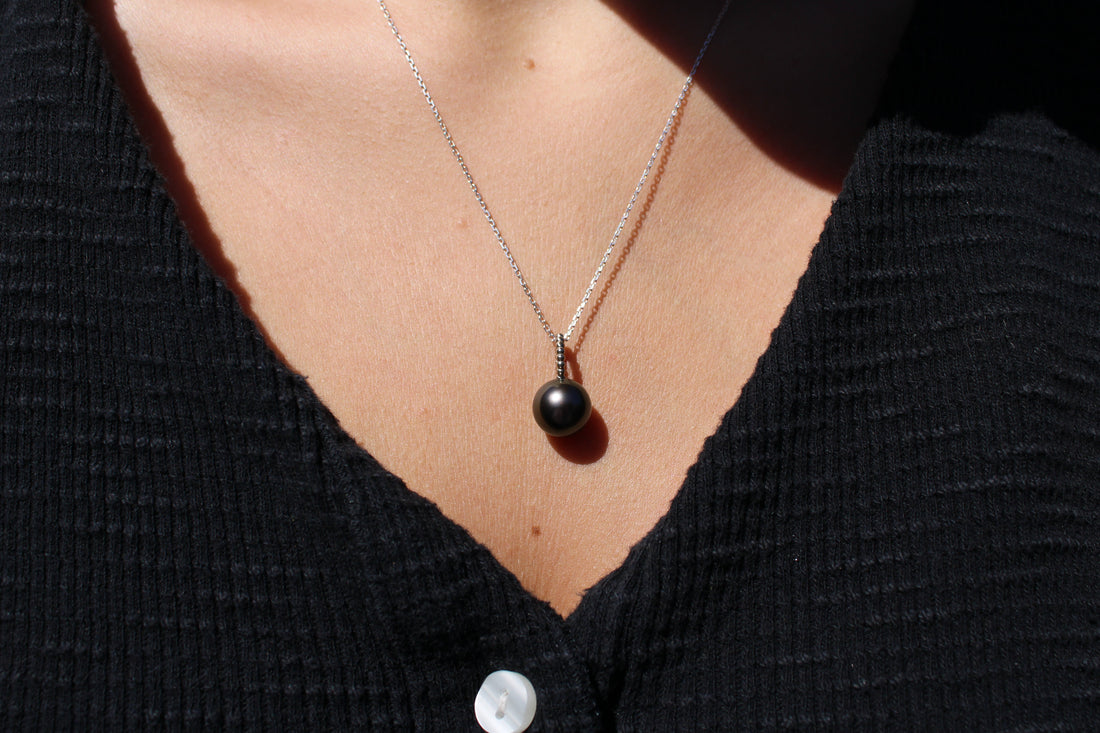 Necklace with a white gold and black pearl pendant worn by a person in a black shirt.