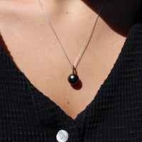 Necklace with a white gold and black pearl pendant worn by a person in a black shirt.